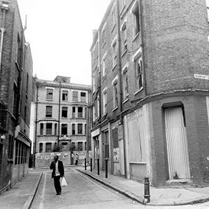 A man carrying his shopping bag as he walks past delapidated buildings with broken