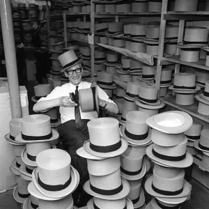 Man happily brushing top hats at a suit hire company in preparation for Royal Ascot Man happily brushing top hats at a suit hire company in preparation for Royal Ascot