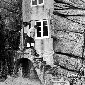 A man looks into the window of a tiny house built into the rocks overlooking the sandy