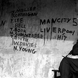 Man sitting on a bench at a bus shelter covered with graffiti after a football match