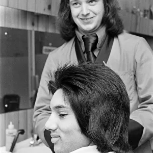 A man who is getting a "Kojak"hair cut. 1975