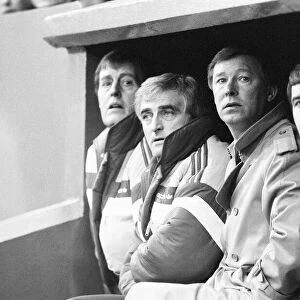 Manchester United manager Alex Ferguson sits in the dugout with coaching staff during