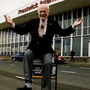 Matthew Hudson sitting on luggage trolly with hands in the air outside Prestwick Airport