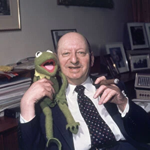 Media Mogul Lew Grade sitting at his desk smoking a cigar while holding Kermit the frog