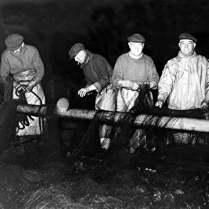 Members of the crew of the Yarmouth drifter Noon Tide mend their nets after being forced