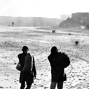 Two men make their way along a beach with their sacks of sea coal that they have