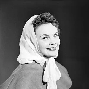 Model Maureen Denham putting on head scarf. July 1956
