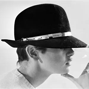 Model Twiggy posing in the studio wearing a black hat and smoking a cigarette