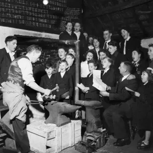 Mr. Simon, smithy and choirmaster, prepares a horseshoe at the anvil while the choir