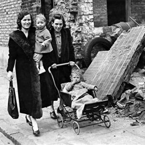 Mrs Applegate (left) and Mrs King with children, walking past a bombed building