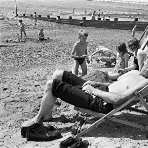 Mum watches the children build sand castles as dad with his knotted handkerchief sun hat