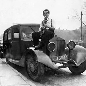 Musician Johnny Roadhouse sitting on the bonnet of a car playing his saxophone