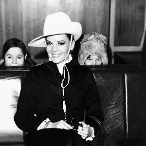 Natalie Wood waits for her flight at London airport peeping pver the seats are her