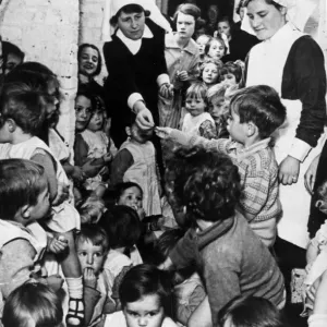 A nursing sister distributes sweets to these young children while they sit in a wine A nursing sister distributes sweets to these young children while they sit in a wine