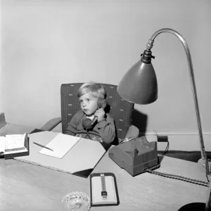 Office Junior: Two year old boy helps out at the offices of Theobald and son. 1957