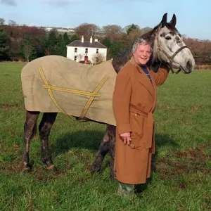 Oliver Reed attore indossa un cappotto marrone lungo, in piedi nel campo con il suo cavallo Bobby a casa. Oliver Reed attore indossa un cappotto marrone lungo, in piedi nel campo con il suo cavallo Bobby a casa.