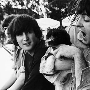 Paul McCartney of The Beatles coddles a puppy watched by John Lennon on the set of Help