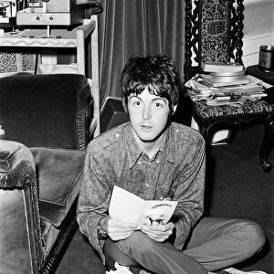 Paul McCartney of The Beatles sitting on the floor cross legged as he opens up birthday