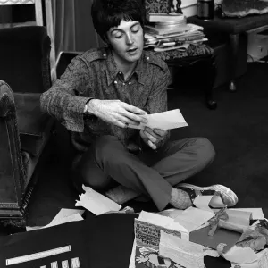 Paul McCartney of The Beatles sitting on the floor cross legged as he opens up birthday