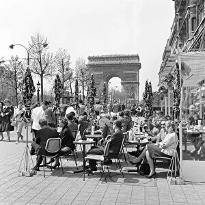 People enjoying the early spring sunshine outside a cafe in Paris near the Arc de