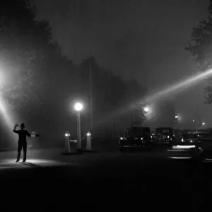 Policeman directing traffic in the fog and dark of a late autumn evening October 1958