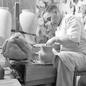 A potter sits at his potters wheel and throws a pot. Circa 1930