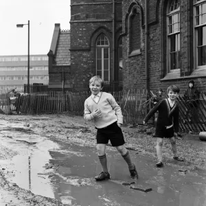 Two pupils of Ross Place School, Ardwick, Manchester, jump across a sea of mud to enter Two pupils of Ross Place School, Ardwick, Manchester, jump across a sea of mud to enter