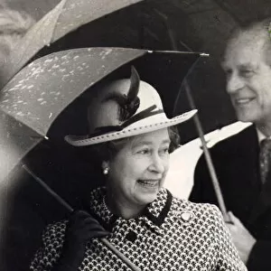Queen Elizabeth II and Prince Philip pictured with umbrellas sheltering from the rain
