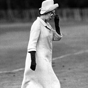 The Queen Elizabeth II walking purposefully across a Polo pitch looking over her