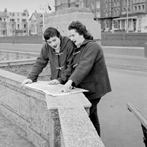 Racing drivers pat Moss and Ann Wisdom aged 21, study their map on the promenade in