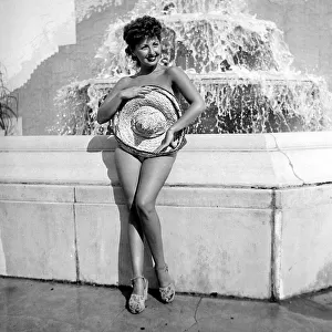 Renee Lester covering herself up with a straw hat as she stands in front of a fountain at
