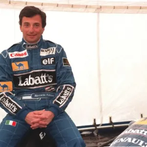 RICARDO PATRESE, MOTOR RACING DRIVER, AT SILVERSTONE SITTING BESIDE CAR WEARING RACING