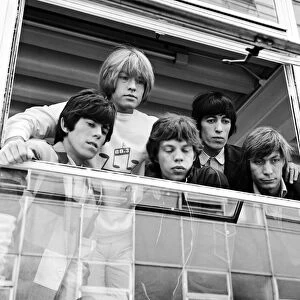 The Rolling Stones looking out of a window at female fans after being in make up before