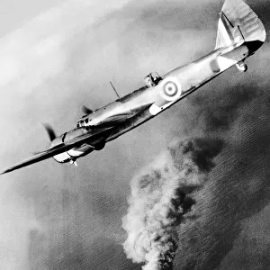 A Royal Air Force Bristol Beufighter aircraft flies over the burning hulk of a