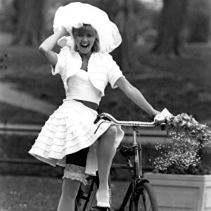 Rubbery Model Jane Sturdy. Wears white outfit, stockings and frilly hat on bicycle