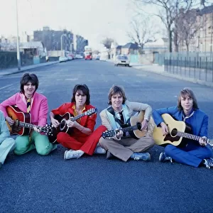 Scottish pop group The Bay City Rollers, sitting in a street holding acoustic guitars