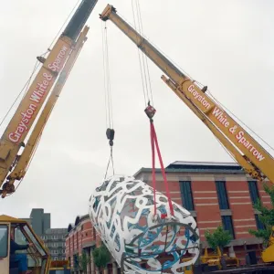 The sculpture Bottle of Notes is lifted off its low loader in the Central The sculpture Bottle of Notes is lifted off its low loader in the Central