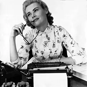 Secretary at typewriter chewing the end of her glasses daydreaming Typist