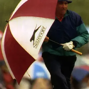 Seve Ballesteros holding a golf umbrella at his side whilst walking to the next hole