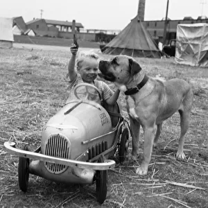 Small boy in his pedal car plays fetch with his pet dog on the South Denes