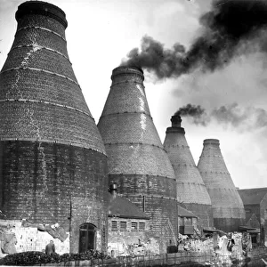 A smokey view with the typical scene of bottle ovens and kilns during the industrial