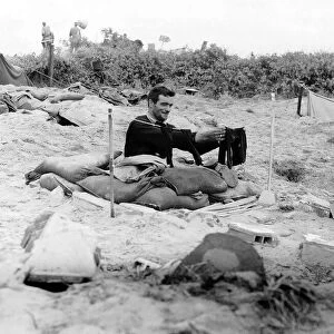 A soldier hangs a pair of socks on a washing line outside his fox hole on a French beach