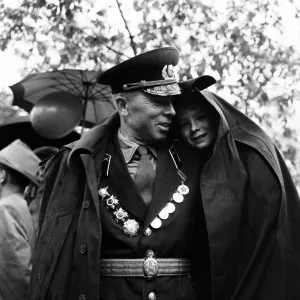 A soldier shelters his son from the rain under his greycoat during the May Day