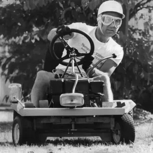Stirling Moss assis sur tondeuse à gazon portant un casque de sécurité. Stirling Moss assis sur tondeuse à gazon portant un casque de sécurité.