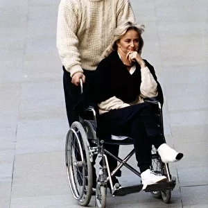Susan George Actress is pushed along in a wheelchair by her husband Simon MacCorkindale