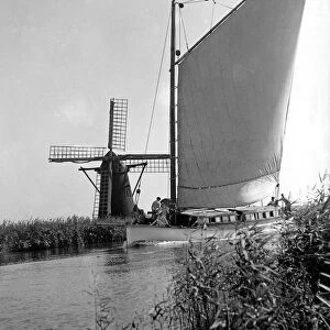 A traditional Norfolk Broad yachts sailing past one of the many windmill water pumps that