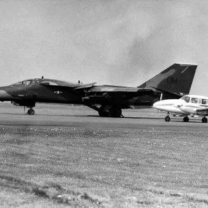 A USAF General Dynamics F-111 Aardvark sits on an airfield next to twin engined civil A USAF General Dynamics F-111 Aardvark sits on an airfield next to twin engined civil