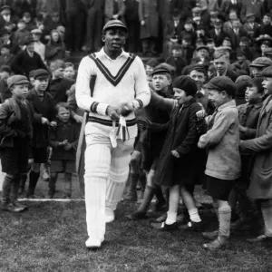 El cricketer de las Indias Occidentales Learie Constantine sale al campo pasando por niños emocionados.