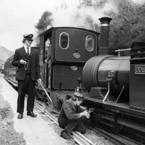 Ein Arbeiter, der ein Öl auf eines der Dampfzüge auf dem Bahnhofsweg der Eisenbahnlinie von Talyllyn anwendet