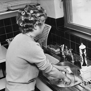 A woman is doing the washing up whislt waiting for her hair to curl before a night